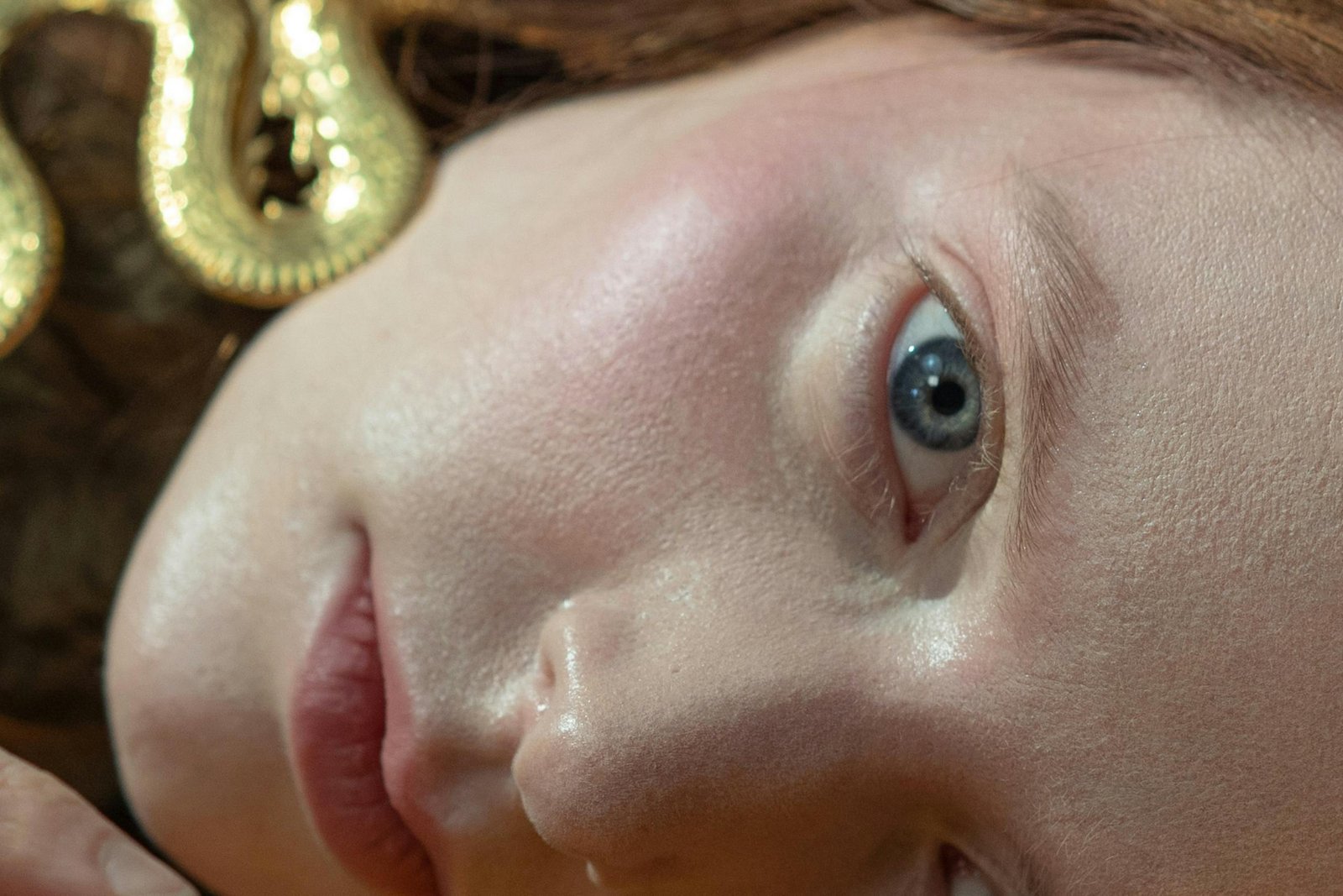 Intimate close-up of a woman's face adorned with a golden snake, capturing delicate beauty and mystery.