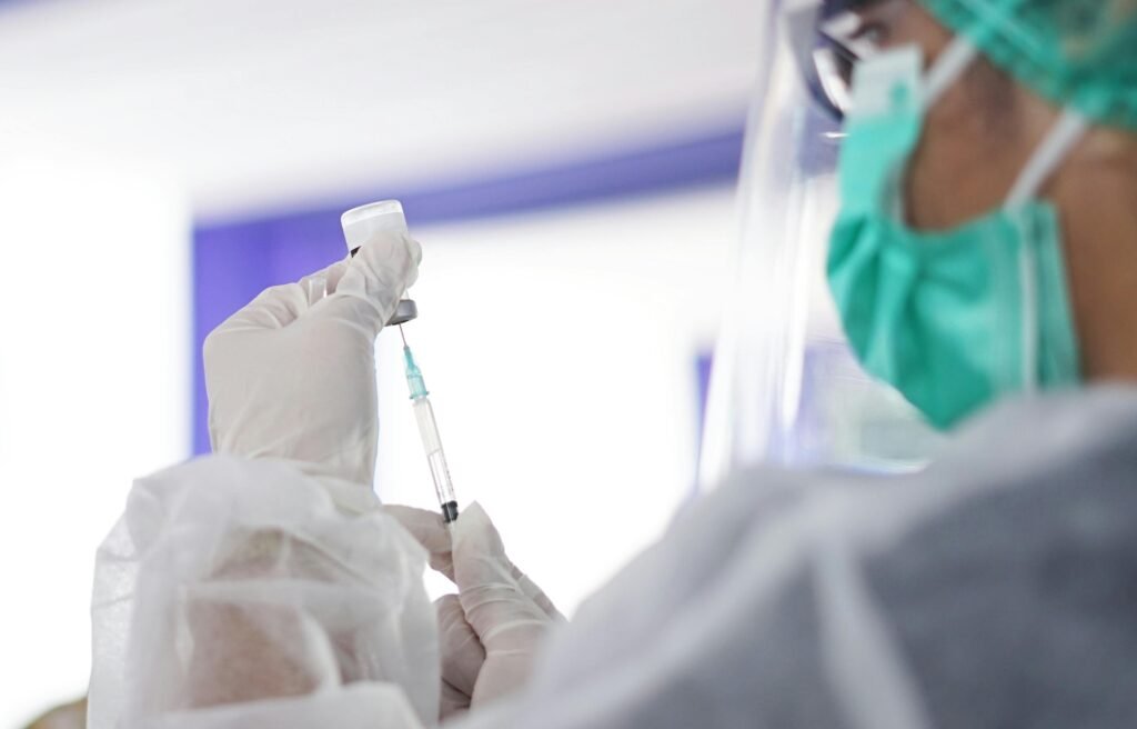 Healthcare worker wearing protective gear drawing vaccine from vial using syringe